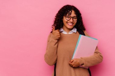 Genç öğrenci ırk kadını pembe arka planda izole edilmiş gülümsüyor ve başparmağını kaldırıyor.