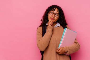 Pembe arka planda soyutlanmış, kuşkulu bir ifadeyle yan bakan genç bir ırk öğrencisi..