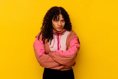 Pembe arka planda soyutlanmış, hoşnutsuzca kaşlarını çatan, kollarını kavuşturan genç melez bir kadın..