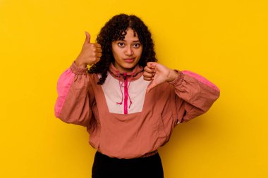 Pembe arka planda soyutlanmış genç melez bir kadın. Baş parmağını kaldırıyor ve onaylıyor. Zor bir seçim.