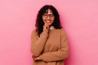 Genç melez kadın pembe arka planda izole edilmiş mutlu ve kendinden emin gülümseyen, elleriyle çenesine dokunan.