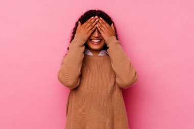 Pembe arka planda soyutlanmış genç bir ırk kadını elleriyle gözlerini kapatıyor, büyük bir gülümsemeyle bir sürpriz bekliyor..