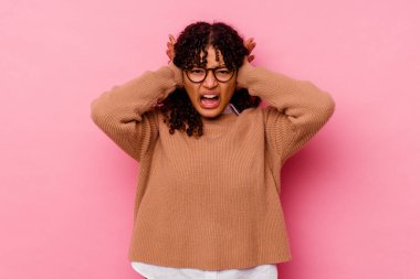 Pembe arka planda izole edilmiş genç bir ırk kadını. Kulaklarını ellerle kapatıyor. Çok fazla ses duymamaya çalışıyor..