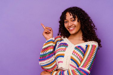 Mor arka planda izole edilmiş genç melez kadın işaret parmağıyla işaret ederek neşeyle gülümsüyor..