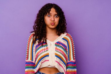 Mor arka planda izole edilmiş genç melez kadın yanakları patlatıyor, yorgun bir ifadesi var. Yüz ifadesi kavramı.