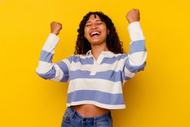 Sarı arka planda izole edilmiş, tasasız ve heyecanlı genç bir ırk kadını. Zafer konsepti.