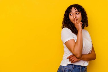 Sarı arka planda izole edilmiş genç melez kadın şüpheli ve şüpheci bir ifadeyle yana bakıyor..