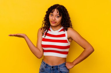 Sarı arka planda izole edilmiş genç melez bir kadın sorgulama sırasında omuz silkiyor ve şüphe duyuyor..