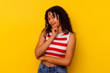 Genç melez kadın sarı arka planda izole edilmiş şüpheli, belirsiz, seni muayene ediyor..