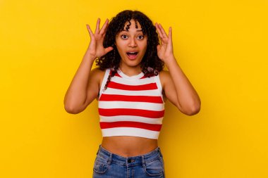 Sarı arka planda izole edilmiş genç melez bir kadın zaferi ya da başarıyı kutluyor, şaşırıyor ve şok oluyor..