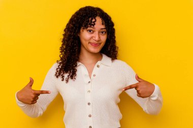 Sarı arka planda izole edilmiş genç bir ırk kadını gömlek fotokopisini elle gösteriyor, gururlu ve kendinden emin.