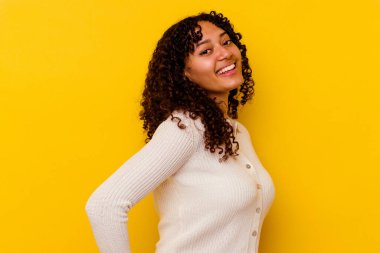 Sarı arka planda izole edilmiş genç, melez bir kadın ellerini kalçasında tutuyor..