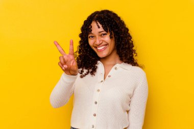 Sarı arka planda izole edilmiş genç melez kadın iki numarayı parmaklarıyla gösteriyor..