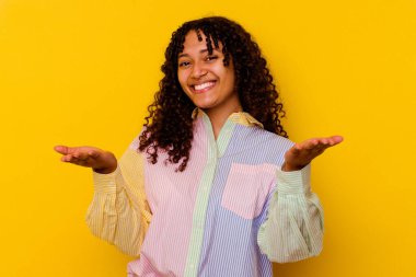 Sarı arka planda soyutlanmış genç melez kadın kollarıyla ölçeği yapıyor, mutlu ve kendinden emin hissediyor..