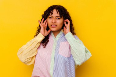Sarı arka planda izole edilmiş, parmaklarıyla kulaklarını kapatan, gürültülü bir ortam tarafından stresli ve çaresiz genç bir ırk kadını..