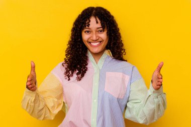 Sarı arka planda izole edilmiş genç bir ırk kadını iki eliyle bir şey tutuyor, ürün sunumu..