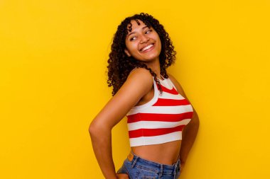 Sarı arka planda yaşayan genç melez kadın mutlu bir şekilde gülüyor ve ellerini karnının üstünde tutarak eğleniyor..