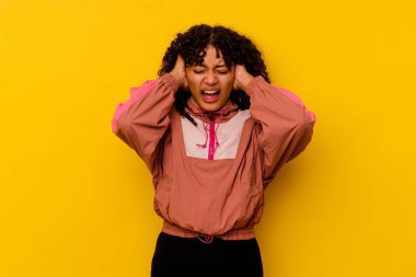 Pembe arka planda izole edilmiş genç bir ırk kadını. Kulaklarını ellerle kapatıyor. Çok fazla ses duymamaya çalışıyor..