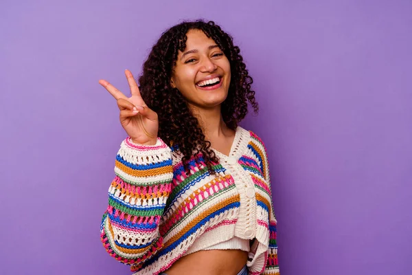 紫色の背景に孤立した若い混合人種の女性喜びと屈託のない指で平和のシンボルを示す — ストック写真