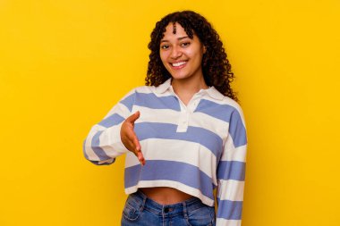 Sarı arka planda izole edilmiş genç bir ırk kadını selamlama jesti olarak kameraya elini uzatıyor..