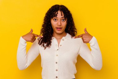 Sarı arka planda izole edilmiş genç melez kadın parmakları aşağıda, olumlu hisler içinde..