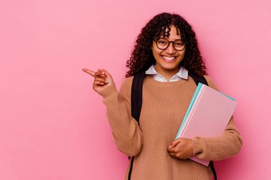 Pembe arka planda izole edilmiş genç, melez bir kadın. Gülümsüyor ve işaret ediyor. Boş alanda bir şey gösteriyor..