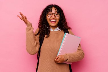 Genç öğrenci melez kadın pembe arka planda izole edilmiş hoş bir sürpriz alıyor, heyecanlı ve el kaldırıyor..