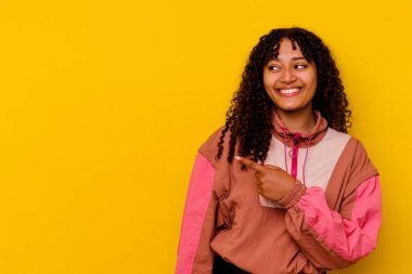 Genç melez kadın pembe arka planda izole edilmiş gülümseyen ve işaret eden boş alanda bir şey gösteriyor..