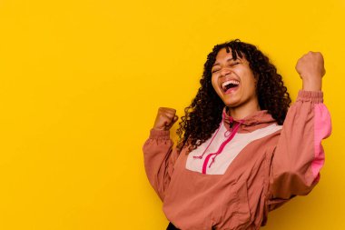 Pembe arka planda soyutlanmış genç melez bir kadın zafer sonrası yumruğunu kaldırıyor, kazanan konsept..