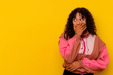 Genç melez kadın pembe arka planda izole edilmiş. Düşünceli bir şekilde bir fotokopi odasına bakıyor. Ağzını eliyle kapatıyor..