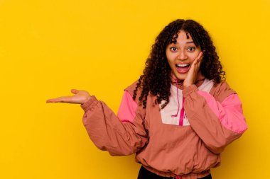 Pembe arka planda izole edilmiş genç melez kadın avuç içinde fotokopi alanı tutuyor, el üstünde tutuyor. Şaşırmış ve mutlu..