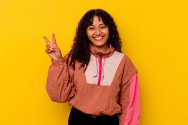 Pembe arka planda izole edilmiş genç melez kadın zafer işareti gösteriyor ve gülümsüyor..