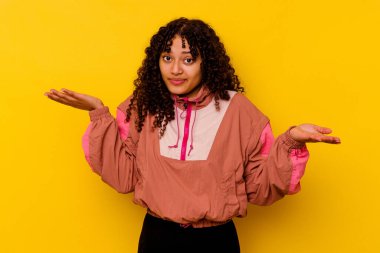 Genç melez kadın pembe arka planda izole edilmiş şüphe içinde ve sorgulama sırasında omuz silkiyor..