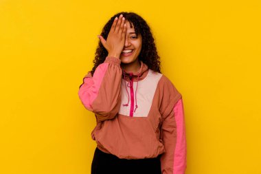 Pembe arka planda izole edilmiş genç melez kadın yüzünün yarısını avuç içiyle kaplayarak eğleniyor..