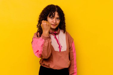 Pembe arka planda izole edilmiş genç bir ırk kadını kameraya yumruk gösteriyor, agresif bir yüz ifadesi..