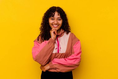 Genç melez kadın pembe arka planda izole edilmiş mutlu ve kendinden emin gülümseyen, elleriyle çenesine dokunan.