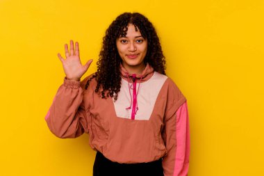Pembe arka planda izole edilmiş genç melez kadın gülümseyerek beş numarayı parmaklarıyla gösteriyor..