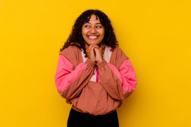 Pembe arka planda soyutlanmış genç melez kadın ellerini çenesinin altında tutuyor, mutlu bir şekilde yana bakıyor..