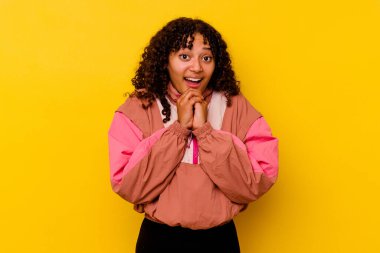 Genç melez kadın pembe arka planda izole edilmiş şans için dua eden, şaşırmış ve ağzını açan..