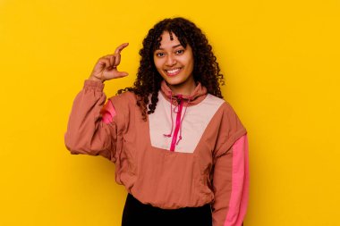 Pembe arka planda izole edilmiş genç melez bir kadın işaret parmaklarıyla küçük bir şey tutuyor, gülümsüyor ve kendinden emin..