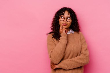 Pembe arka planda izole edilmiş genç melez kadın şüpheli ve şüpheci bir ifadeyle yana bakıyor..