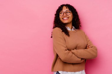 Pembe arka planda soyutlanmış genç melez bir kadın kollarını kavuşturarak gülümsüyor..