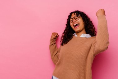 Pembe arka planda soyutlanmış genç melez bir kadın zafer sonrası yumruğunu kaldırıyor, kazanan konsept..