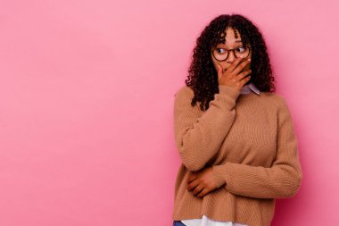 Genç melez kadın pembe arka planda izole edilmiş. Düşünceli bir şekilde bir fotokopi odasına bakıyor. Ağzını eliyle kapatıyor..