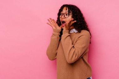 Pembe arka planda soyutlanmış genç melez kadın yüksek sesle bağırıyor, gözleri açık ve elleri gergin tutuyor..