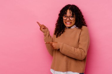 Pembe arka planda izole edilmiş genç melez kadın işaret parmağıyla fotokopi alanını işaret ederek şok oldu..