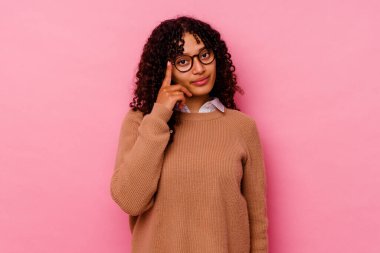 Pembe arka planda izole edilmiş genç melez bir kadın şakağı parmağıyla işaret ediyor, düşünüyor ve bir göreve odaklanıyor..