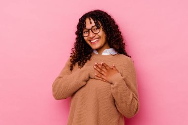 Pembe arka planda izole edilmiş genç melez bir kadın. Dostane bir ifadeye sahip. Avuç göğse bastırıyor. Aşk konsepti.
