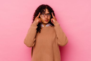 Pembe arka planda izole edilmiş genç melez kadın bir göreve odaklanmış, işaret parmaklarını işaret ediyor..