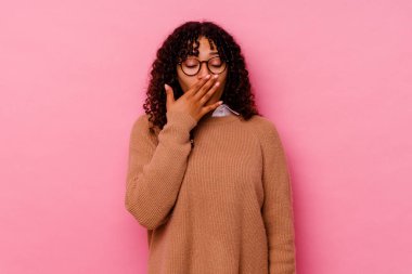 Pembe arka planda soyutlanmış genç melez bir kadın esniyor. Ağzıyla ağzını kapatan yorgun bir hareket sergiliyor..